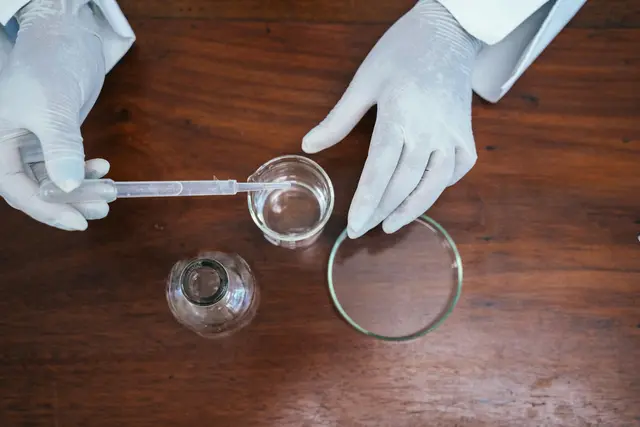 Person in a lab coat using a syringe to transfer a liquid